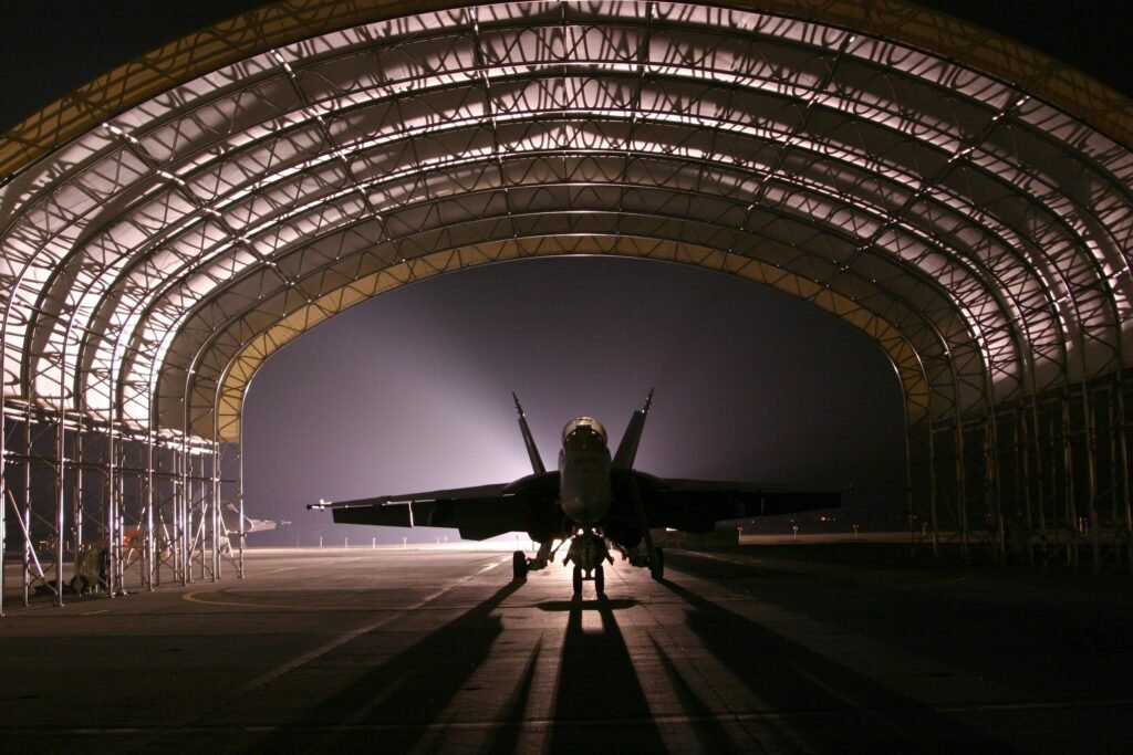 Silhouetted fighter jet in an illuminated hangar at night creates a dramatic scene.